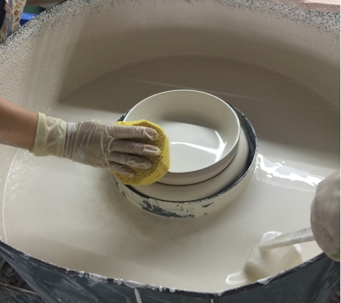 A worker is pouring glaze into a ceramic dish..png